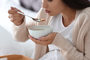 A young woman eating soup after dental implant surgery