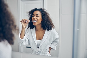 A woman brushing her teeth in front of a bathroom mirror
